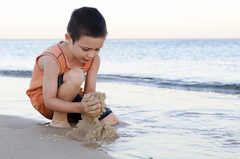 Deček se igra na plaži v poznih popoldanskih urah - simbolna slika za članek o vročinskih krčih