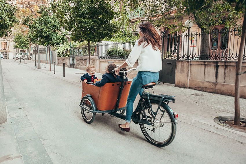 Bakefiets - nizozomsko kolo, s katerim mama prevaža svoje 3 otroke v veliki čkatli nad sprednjim kolesom.