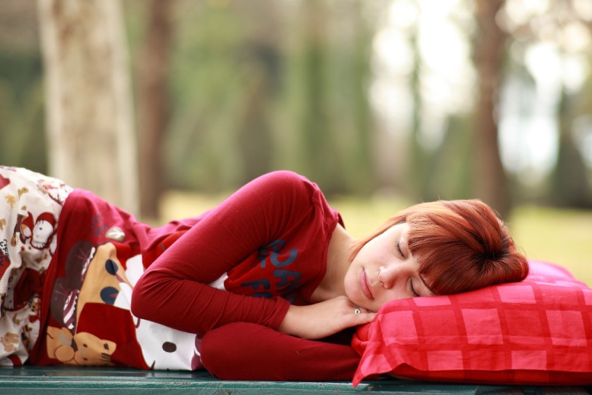 Mlada ženska na rdečem vzglavniku spi mirno, kot bi spala v naravi. Simbolna slika za dober spanec.