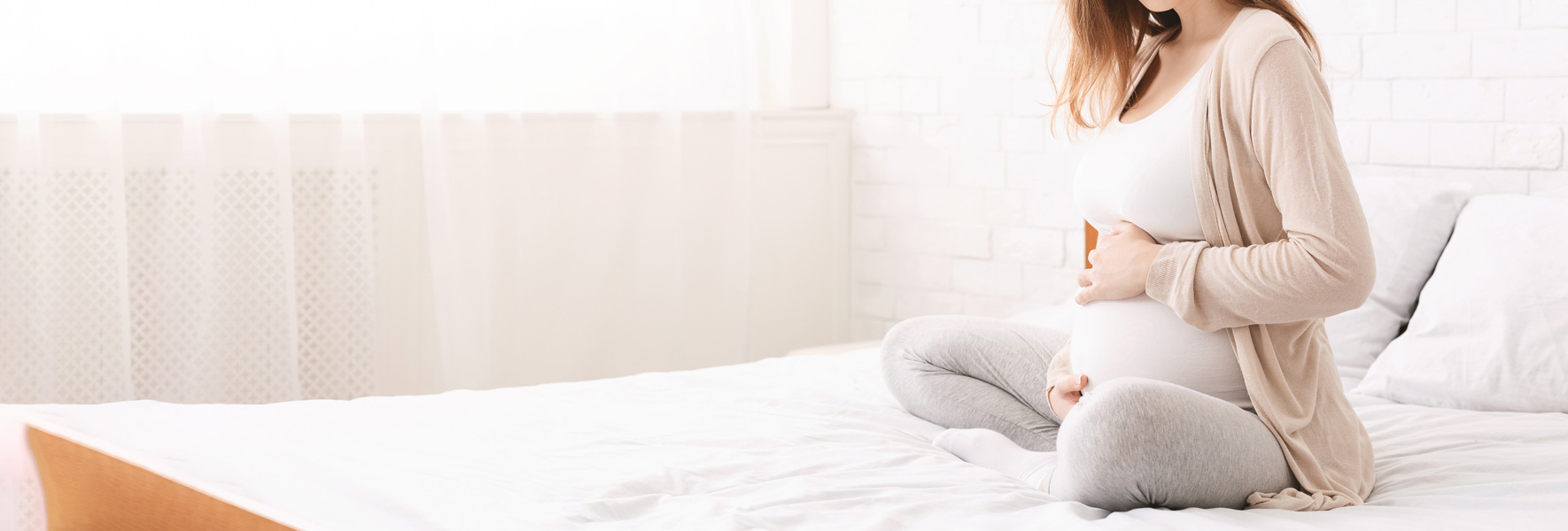 Nosečnica sedi na postelji in objema svoj trebušček