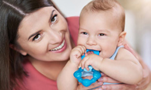 Mamica drži dojenčka, ki si dlesni masira z grizalom