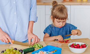 Malčica ob mami zavzeto reže sadje