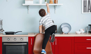 Deček s pomočjo stola pleza na pult proti polički s sladkarijami