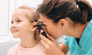 Zdravnica gleda malčici v uho in preverja vnetje