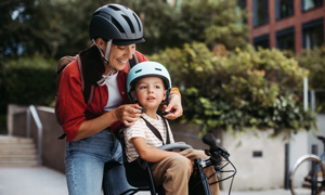 Mama malčici na kolesu pripenja čelado - simbolna slika za zavarovanje za kolo