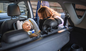 Mama privezuje dojenčka v otroški sedež v avtu