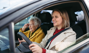 Zavarovanje prehodne oskrbe vam nudi tudi pomoč pri prevozih - mlajša negovalka na sliki na pregled pelje starejšo oskrbovanko.