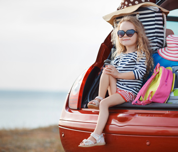 Deklica sedi v prtljažniku, polnem prtljage, ki so jo starši pakirali brez stresa