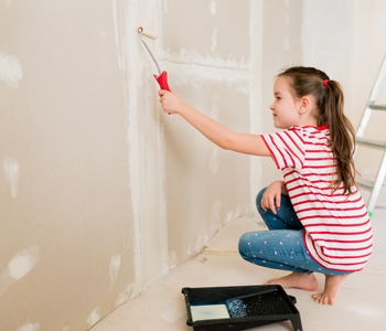 Deklica čepi pri steni in zakriva razpoke v njej – otroci naj pri prenovi otroške sobe sodelujejo, če le lahko.