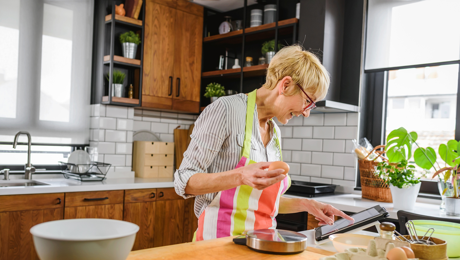 Starejša gospa v kuhinji pripravlja obrok s pomočjo recepta, ki ga je našla na spletu