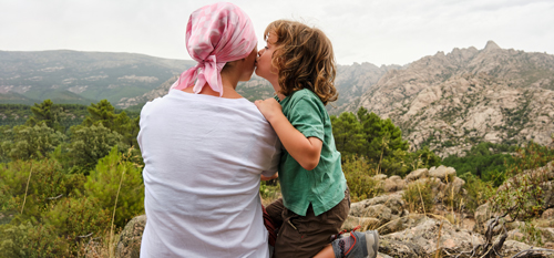 Mati z ruto na splehodu v hribih - otrok ji daje poljubček na lice. Simbolna slika za zavarovanje Raki.