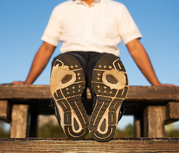 Tekač se po treningu razteza in zato so v fokusu slike podplati njegovih tekaških čevljev.