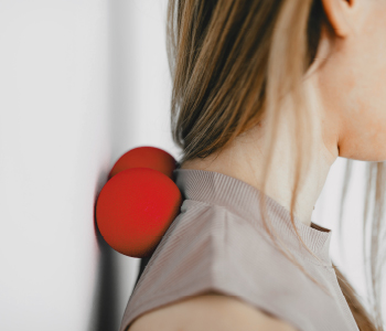 Mlada športnica poskuša razbremeniti bolečino v križu z masažnim valjem na vratu.