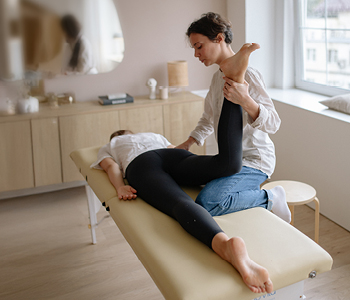 Ženska na fizioterapiji, fizioterapevtka preverja gibljivost njenih sklepov in togost mišic, ker ima bolečine pri teku.