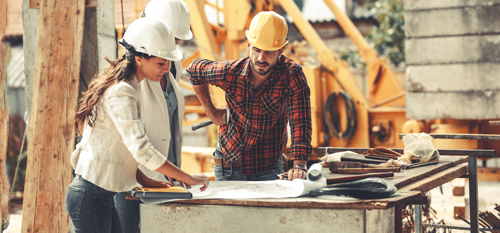 Gradbenik in investitor na gradbišču pregledujeta načrte dela.