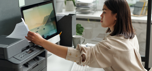 Zaposlena v pisarni pregleduje natiskane dokumente - brez elektronskih naprav bi težko opravljala svoje delo