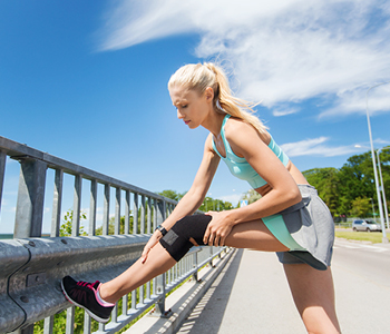 Mlado dekle med tekom po mestu razteguje mišice in se ukvarja z bolečninami v kolenu.
