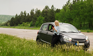 Ženska gleda pod pokrov vozila v motor, ker se ji je avto pokvaril sredi ceste