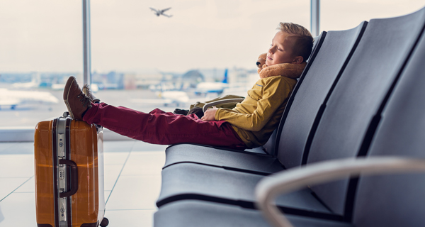Deček spi v letališki čakalnici z nogami na kovčku - simbolna slika za zavarovanje odpoved potovanja