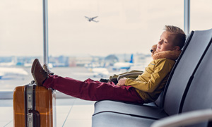 Deček na letališču mirno čaka, brez skrbi, da bi moral uporabiti zavarovanje odpovedi potovanja.