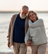 Starejši par uživa na sprehodu ob morju, ki jima ga omogoča finančna stabilnost zaradi pokojninskega varčevanja.