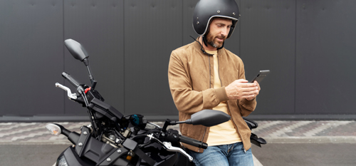 Motorist med oddihom sloni na motorju in s čelado na glavi uporablja klepet na telefonu