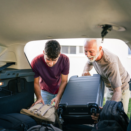 Oče pomaga odraslemu sinu naložiti prtljago v avto, ko se odpravlja na potovanje
