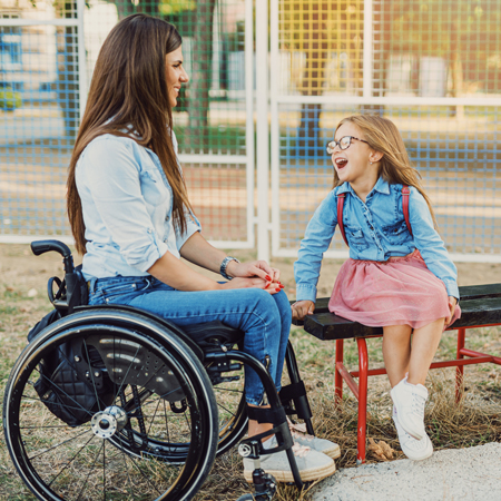 Deklica z mamo v invalidskem vozičku uživa v lepem dnevu na igrišču