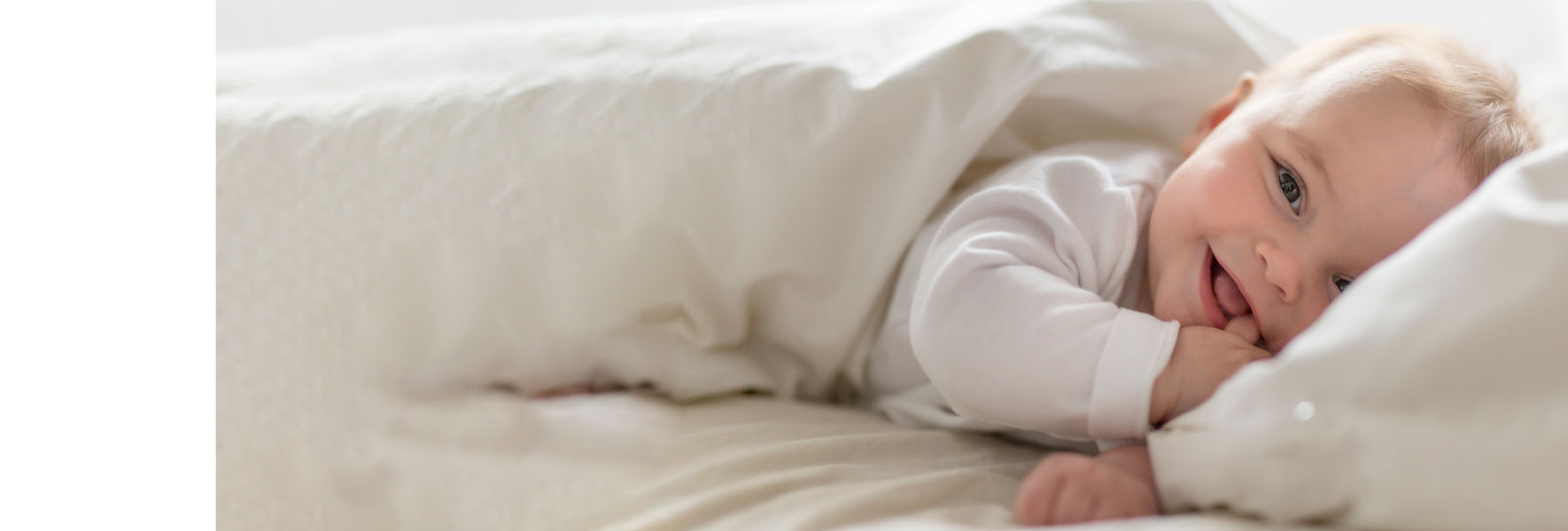 Ljubek dojenček s prstom v ustih se smeje v kamero